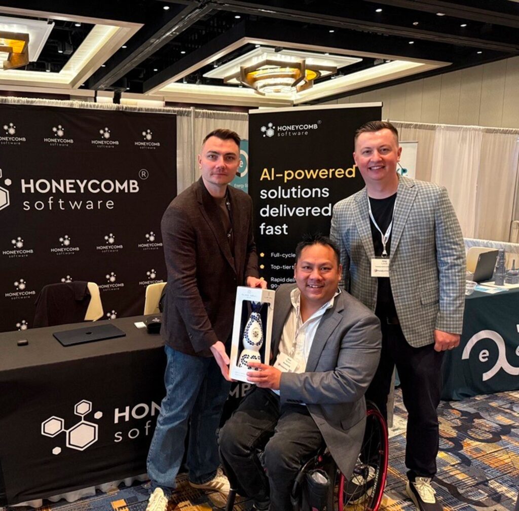 Honeycomb Software team members posing at their event booth, with one attendee holding a decorative tequila decanter gifted during the conference.