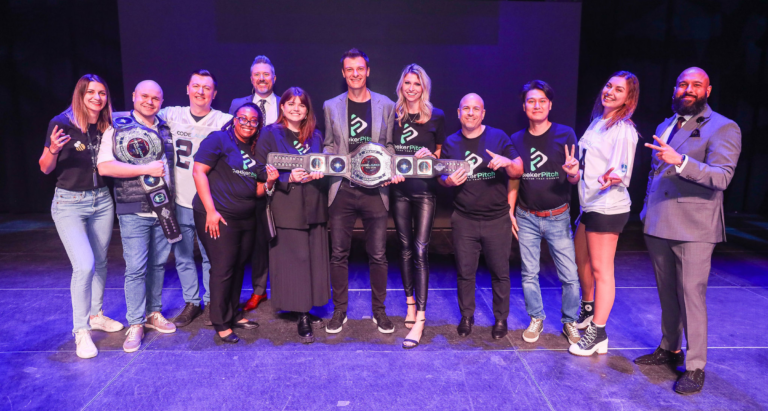 Team from Honeycomb Software celebrating on stage with championship belts after winning CodeLaunch HOU for the second time in a row